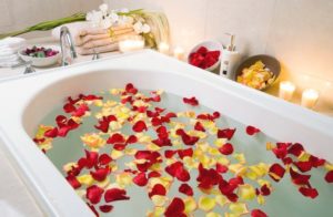 bath filled with red and yellow flower petals and with candles nearby