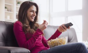 woman on leather couch with popcorn and remote in each hand