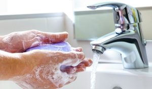 two hands being lathered with soap next to running sink faucet