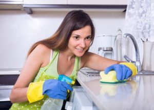 woman in green top with cleaning gloves scrubbing down kitchen