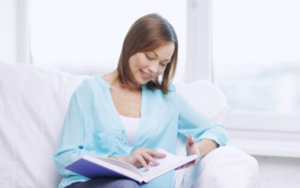 woman in light blue top reading book on white couch in white room