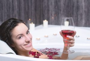 woman in bath holding up glass of red wine