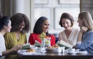 five women discussing book at a table